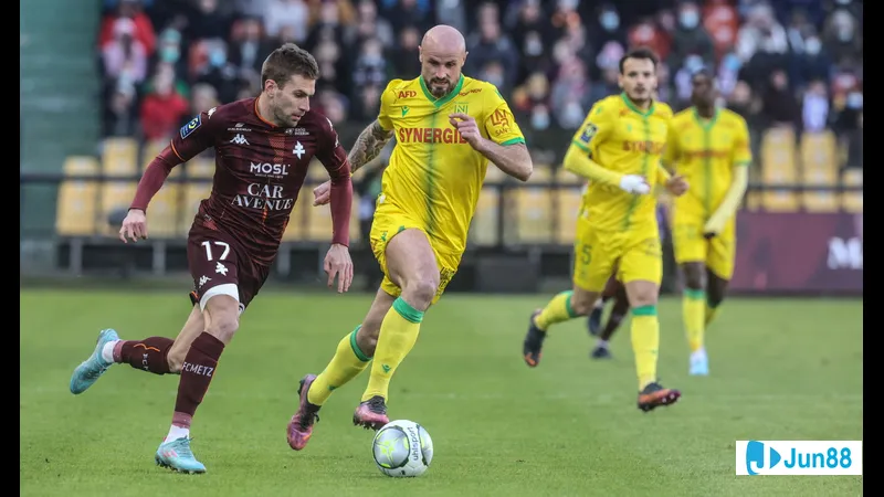 Cầu thủ của Nantes đang vượt qua cầu thủ của Metz trên sân cỏ Cầu thủ của Nantes đang vượt qua cầu thủ của Metz trên sân cỏ